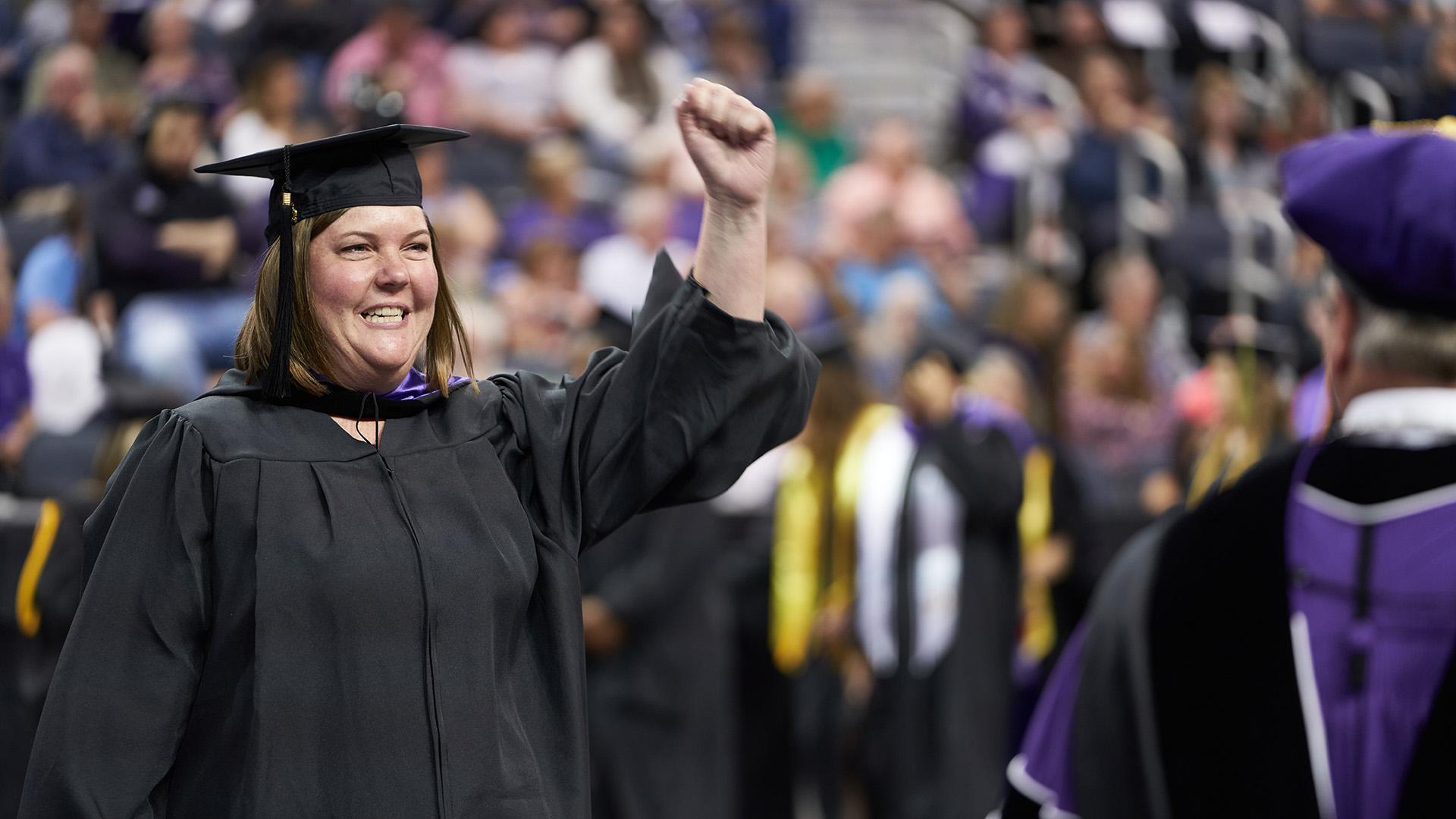 UE adult graduate with hand up at commencement